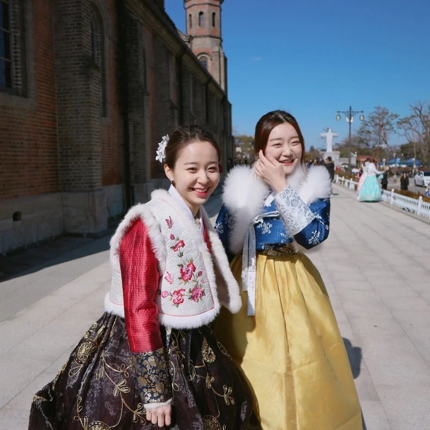 Two models in winter hanbok smiling outdoors