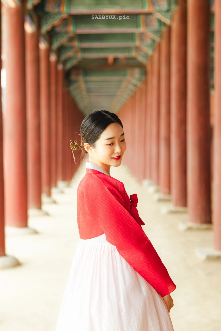 A portrait in a red and white hanbok along a colonnade