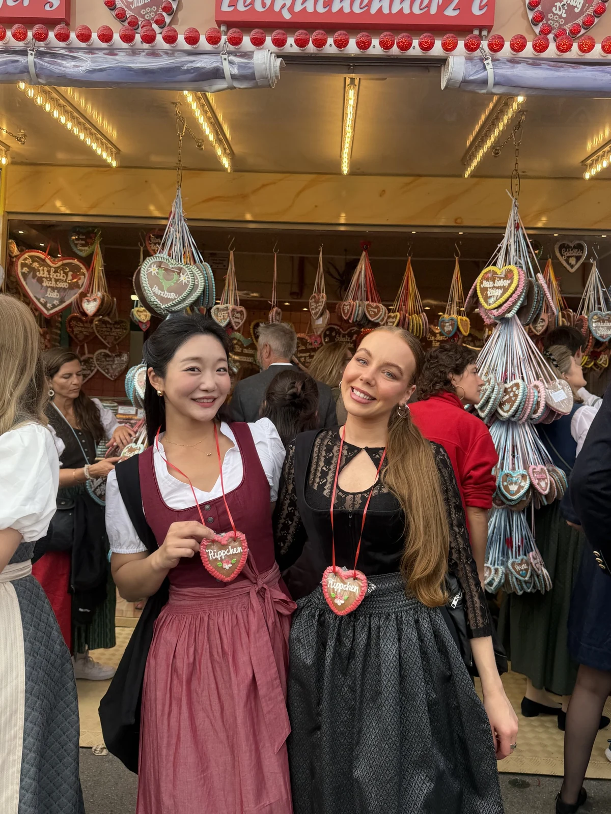 Two people in festival dresses beside a stall displaying heart-shaped gingerbread cookies